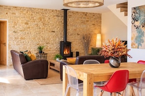 Una sala de estar acogedora con una pared de piedra, una chimenea, una mesa de comedor con sillas y una escalera.