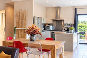 A modern kitchen with a wooden dining table, red chairs, and a vase of dried flowers.