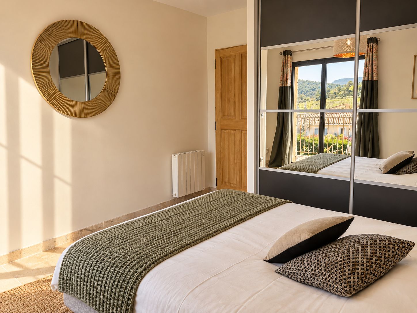 A bedroom with a bed, a window with a view, a radiator, and a mirror on the wall.