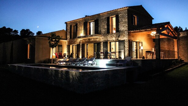 A two-story house with a stone facade, large windows, and a balcony with outdoor seating.