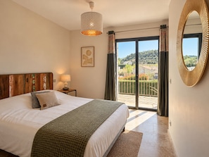 Un dormitorio con cama, lámpara de noche, vista al exterior a través de una puerta corrediza y un espejo grande en la pared.