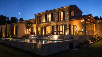 A two-story stone house with a swimming pool and outdoor seating area.