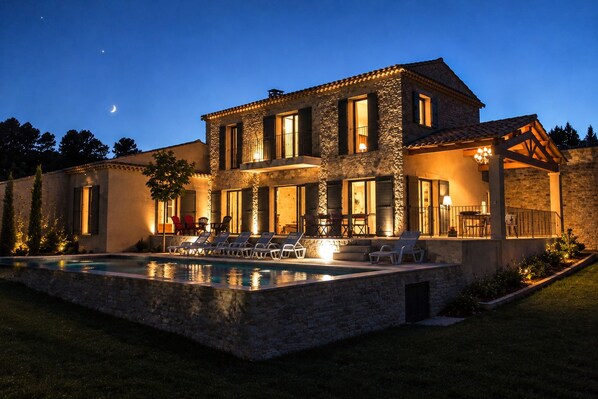 A two-story stone house with a swimming pool and outdoor seating area.