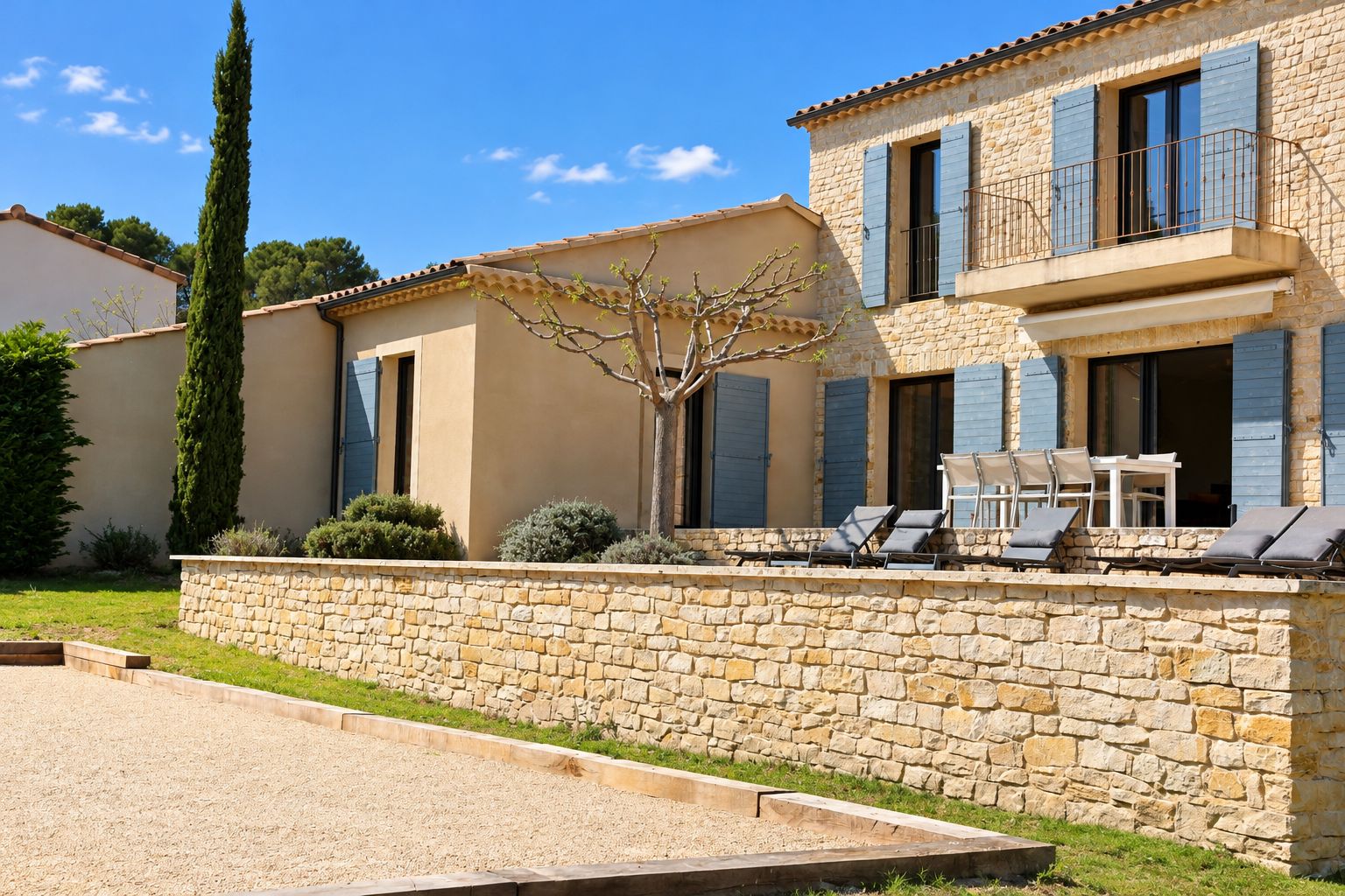 A two-story stone house with a balcony, outdoor seating, and a well-maintained garden.