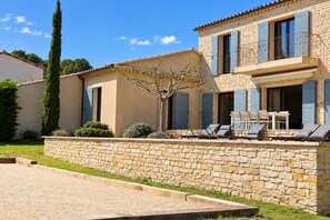 A two-story stone house with a balcony, outdoor seating, and a well-maintained garden.