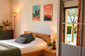 Un dormitorio con cama, mesita de noche, lámpara, ventana con vista a una piscina y dos carteles en la pared.