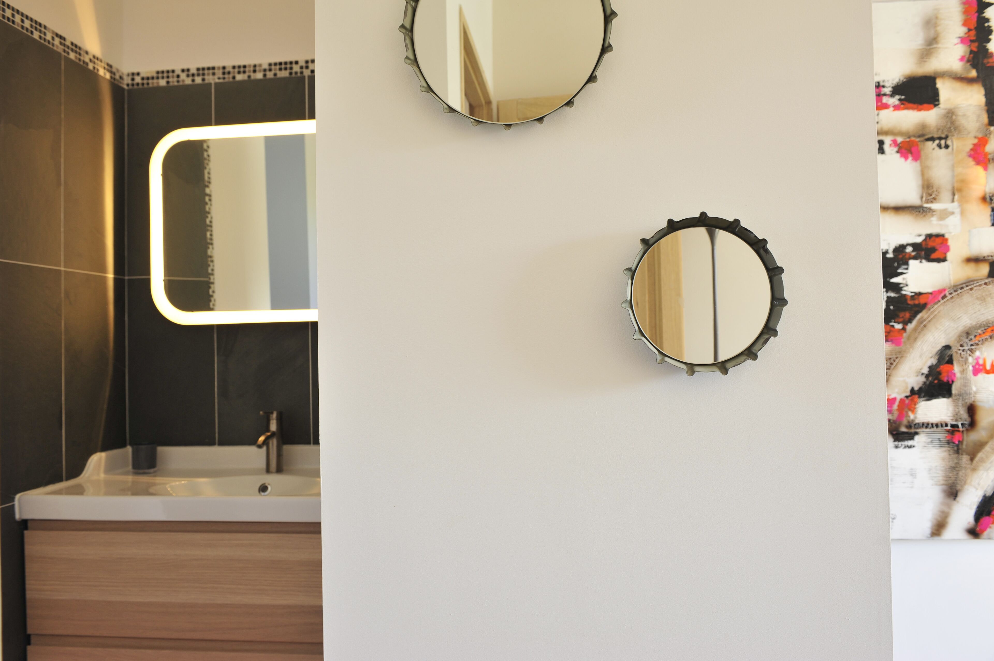 Un baño con diseño moderno, que incluye un espejo grande, un lavamanos y un adorno en la pared.
