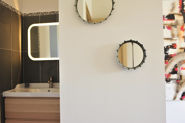 Un baño con diseño moderno, que incluye un espejo grande, un lavamanos y un adorno en la pared.