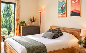 Una cama bien hecha con almohadas estampadas, una lámpara de noche y vistas a árboles a través de una ventana.