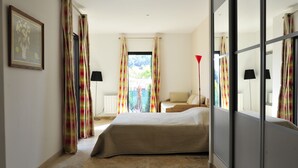 A hotel room with a bed, a window with curtains, a lamp, and a painting on the wall.