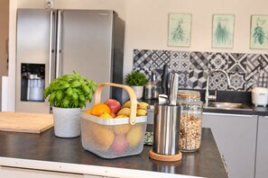 A kitchen counter with a fruit basket, a knife holder, a plant, and a refrigerator.