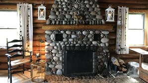 L’intérieur d’un chalet rustique, avec une cheminée en pierre, des poutres en bois et un coin salon confortable.