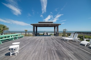 Une terrasse en bois agrémentée d’un belvédère, de tables de pique-nique et de chaises longues, le tout offrant une vue sur l’océan.