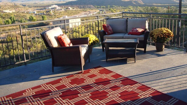 A balcony with wicker furniture, a red patterned rug, and a potted plant.