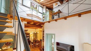 Un interior de varios niveles con una escalera, un comedor y una sala de estar con televisor.