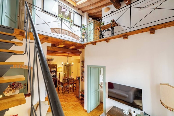 A multi-level interior with a staircase, a dining area, and a living room with a TV.