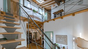 Una escalera de madera de varios niveles con barandilla metálica, un comedor con candelabro y un mapa en la pared.