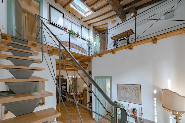 Un escalier en bois à plusieurs niveaux avec une rampe en métal, un coin repas agrémenté d’un lustre et une carte accrochée au mur.