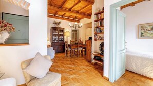 Una sala de estar acogedora con piso de madera, un sofá, un comedor con mesa y sillas, y una estantería.