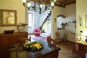 Un coin repas avec une table en verre, des chaises en bois, un plateau de fruits, un vase rempli de fleurs et un escalier menant à une autre pièce.