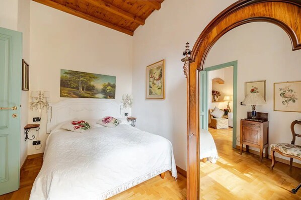 Une chambre avec un grand lit, des poutres apparentes en bois au plafond, une porte en bois et un miroir.