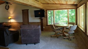 Habitación acogedora con paredes y techo de madera, un televisor de pantalla plana en la pared, una mesa de comedor con sillas, un sofá y una lámpara.
