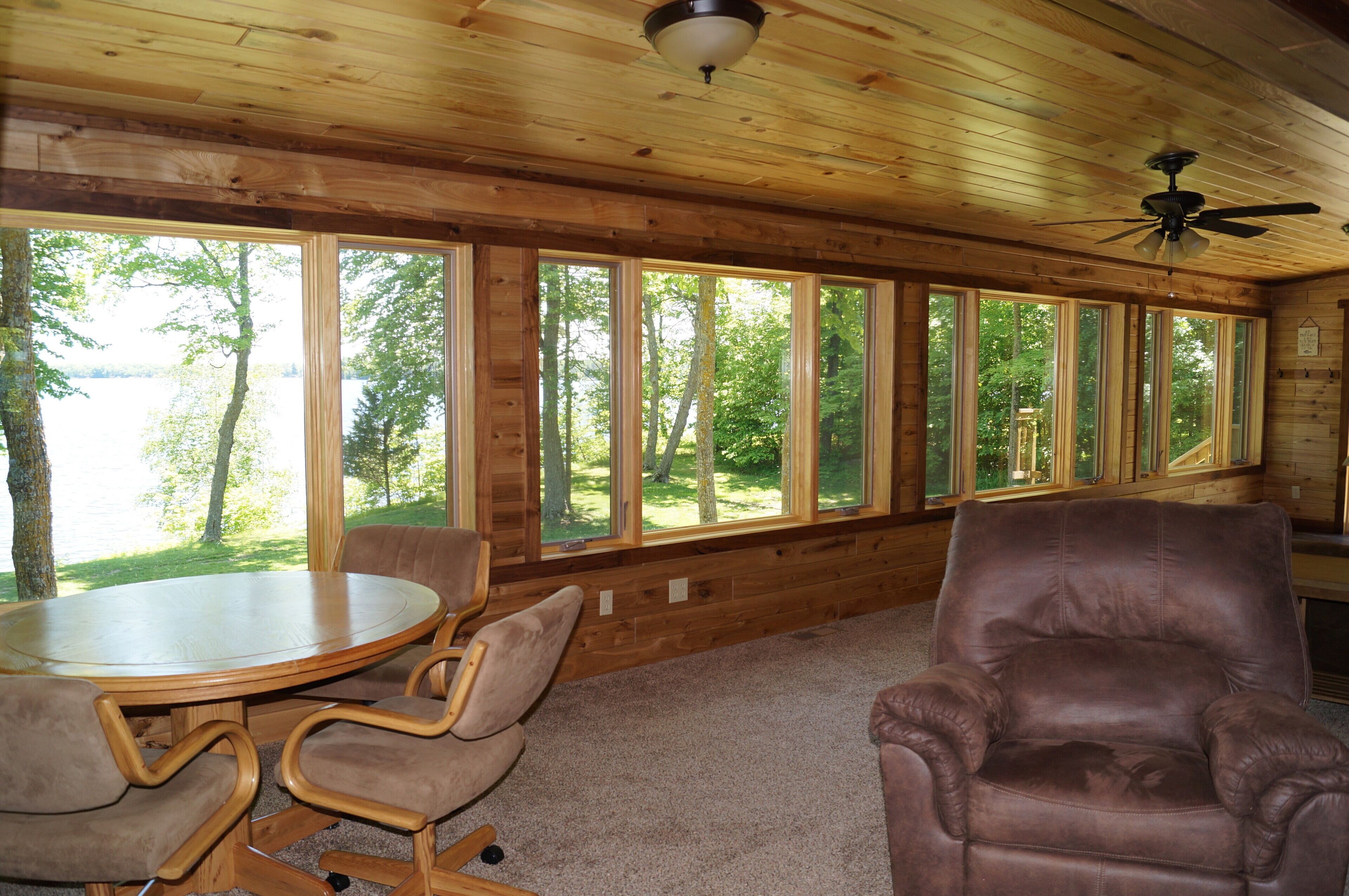 L’intérieur d’un chalet en bois, avec un grand mur vitré, une table ronde et deux fauteuils en cuir.