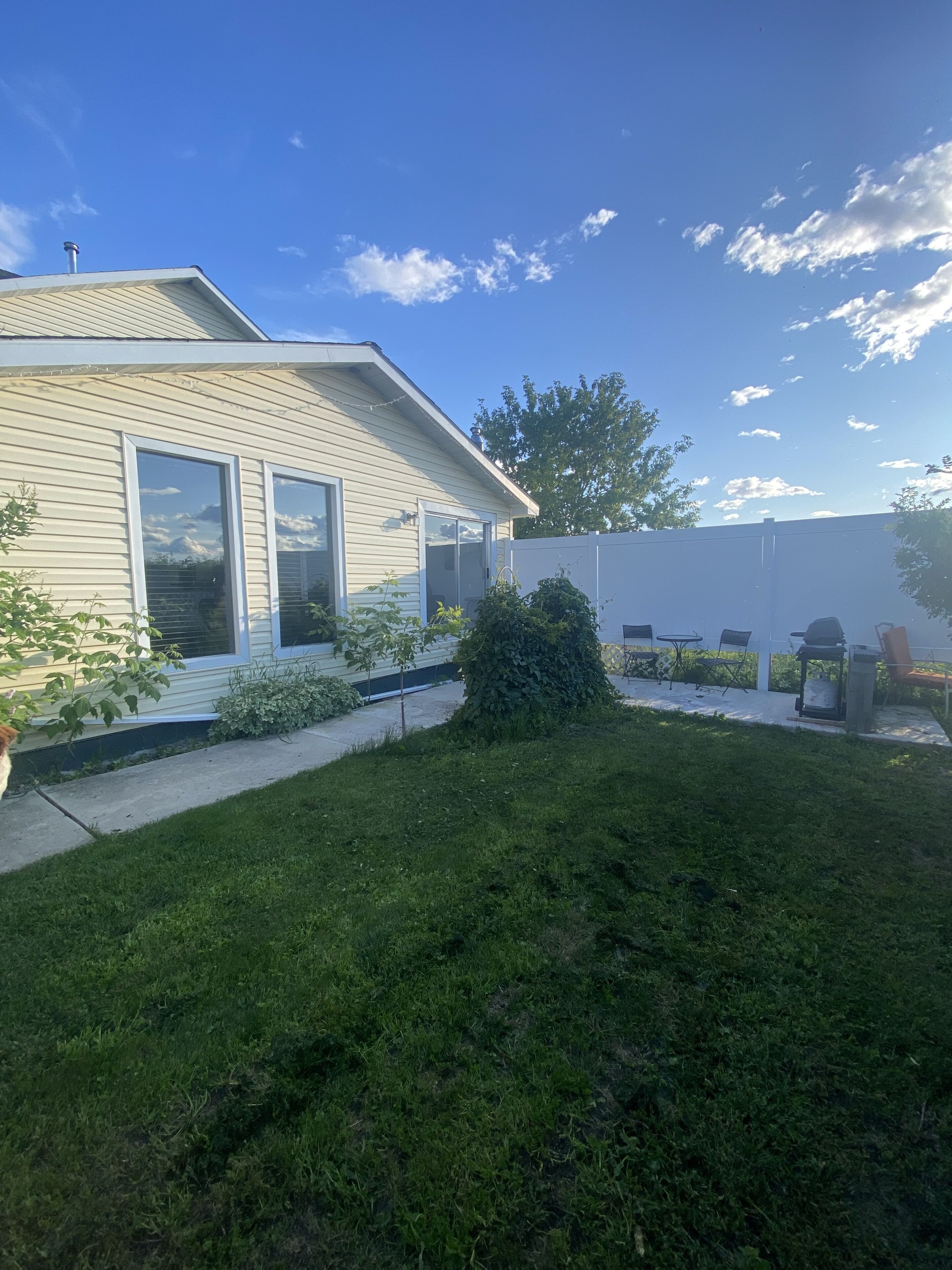 A house with a front yard, a small patio with outdoor furniture, and a tree.