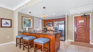A modern kitchen with a central island, bar stools, stainless steel appliances, and wooden cabinets.