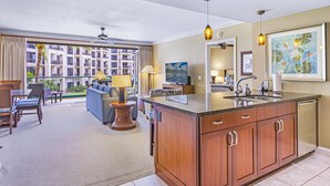 A hotel room with a large window, a balcony, a kitchenette, and a living area with a sofa and a TV.