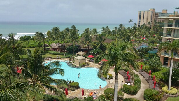 A resort with a central swimming pool surrounded by palm trees and a view of the ocean.
