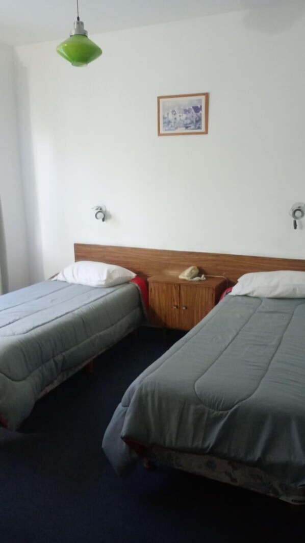 A room with two beds, a wooden headboard, a small wooden nightstand, a telephone, and a framed picture on the wall.