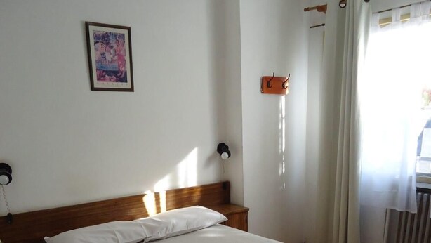 A neatly made bed in a room with a wooden headboard, a bedside table with a lamp, a framed picture on the wall, and a window with curtains. - Residencial Ski (Esquel)