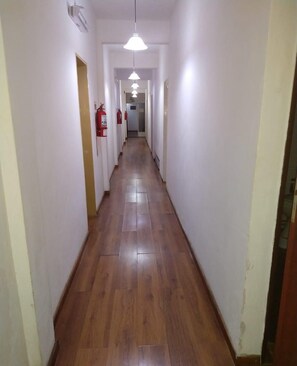 A long, narrow hallway with wooden flooring and white walls. There are ceiling lights and fire extinguishers visible. - Residencial Ski (Esquel)