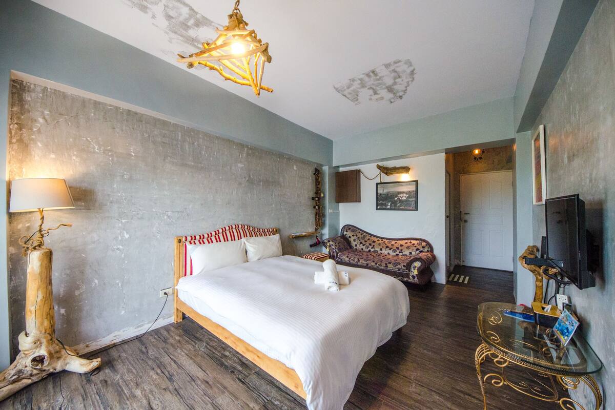A bedroom with a large bed, a sofa, a television, and a wooden floor.
