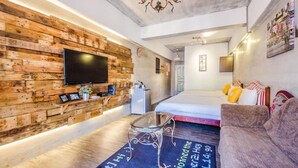 A modern living room with a wooden wall, a flat-screen TV, a glass coffee table, a sofa, and a bed with colorful pillows. - Lunasea Apartment (Hengchun)