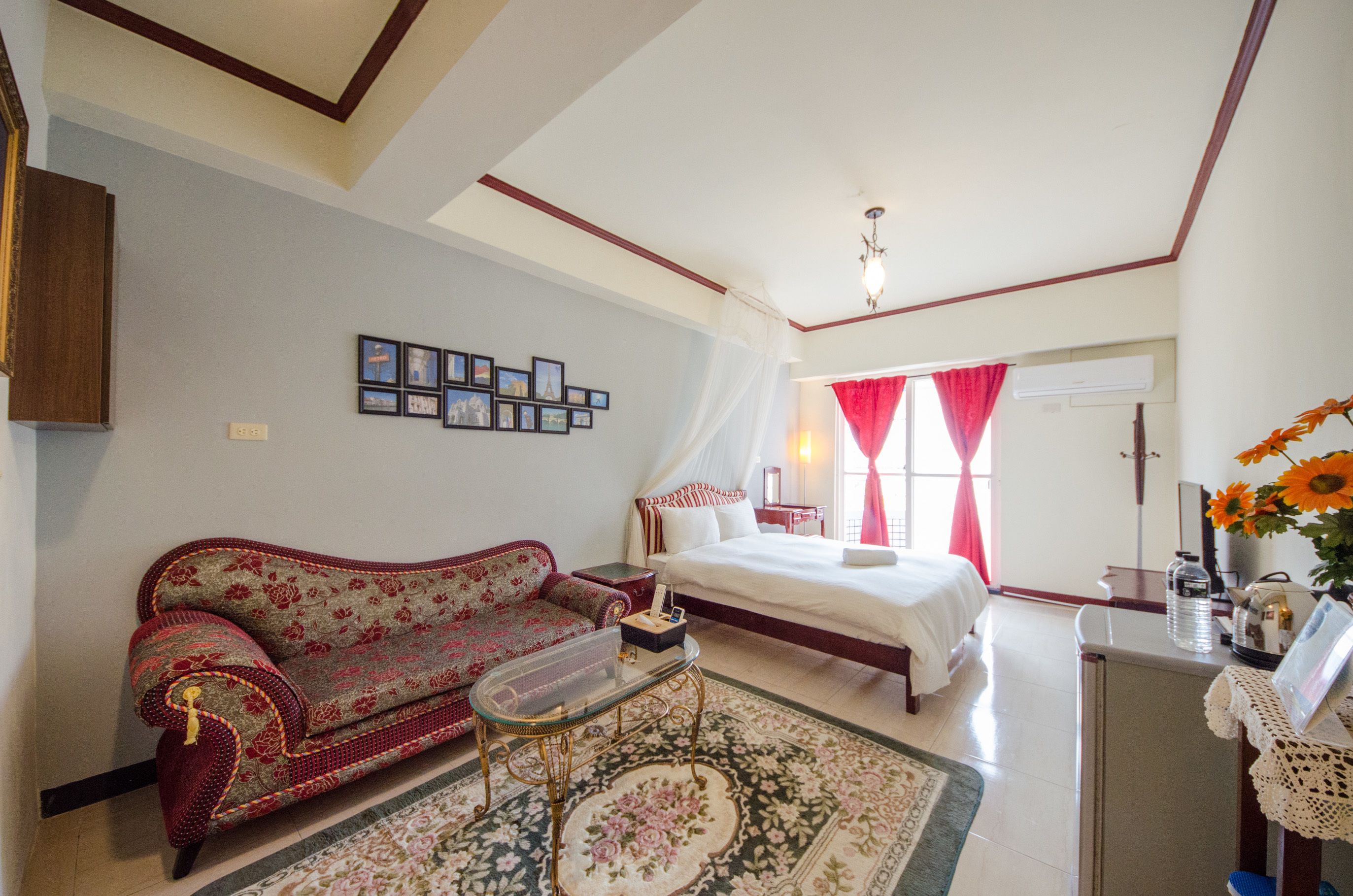A bedroom with a bed, a sofa, a bedside table, a mirror, and a window with curtains.