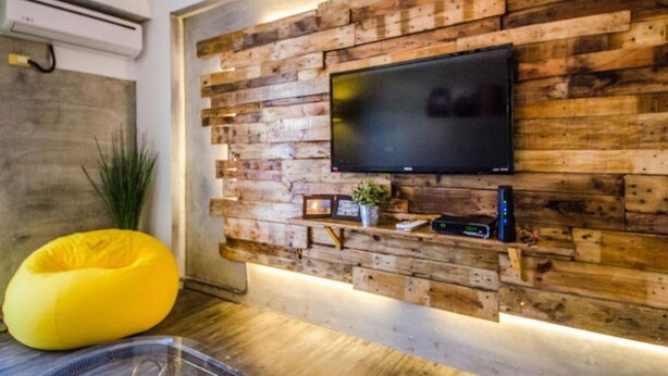 A modern living room with a wooden wall panel, a flat-screen TV, a yellow bean bag, and a small shelf with decorative items. - Lunasea Apartment (Hengchun)