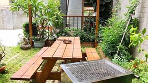 A wooden picnic table with a grill in a garden area with potted plants and a brick wall. - The Colors Under The Sea (Hengchun)
