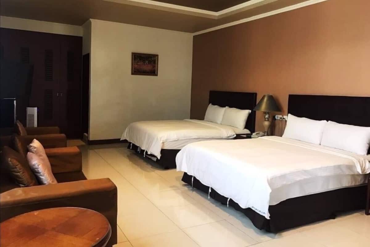 A hotel room with two beds, a sofa, a small table, and a painting on the wall.