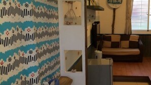 A small, cozy room with a sofa, a bed, a window with curtains, and a wall with a patterned design. - Landscape Rural B&B (Checheng)