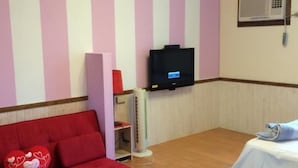 A room with a red sofa, a white table with a blue tablecloth, a TV mounted on the wall, and a window with curtains. - Landscape Rural B&B (Checheng)