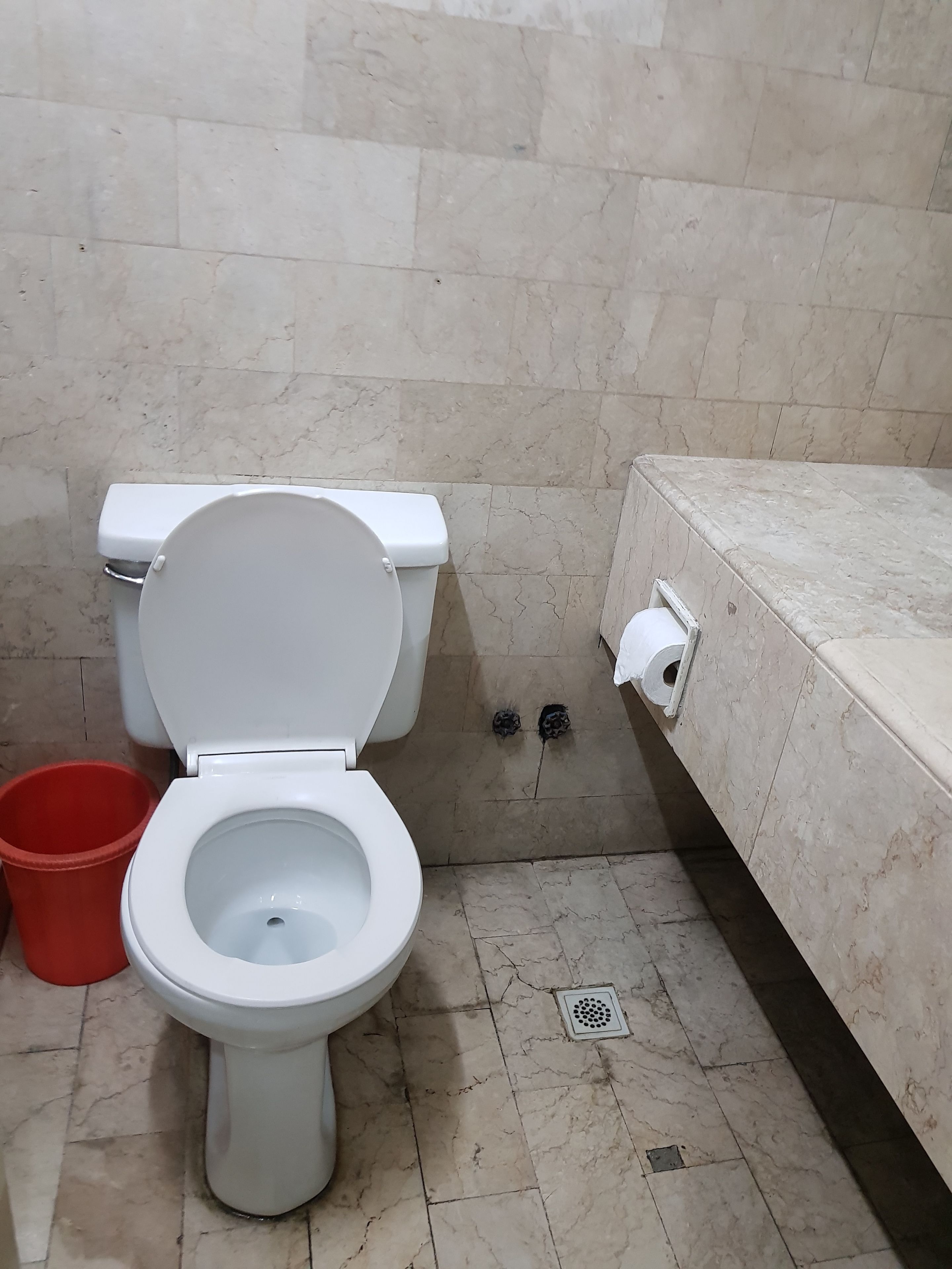 Een badkamer met een toilet, een rode emmer en een marmeren vloer.