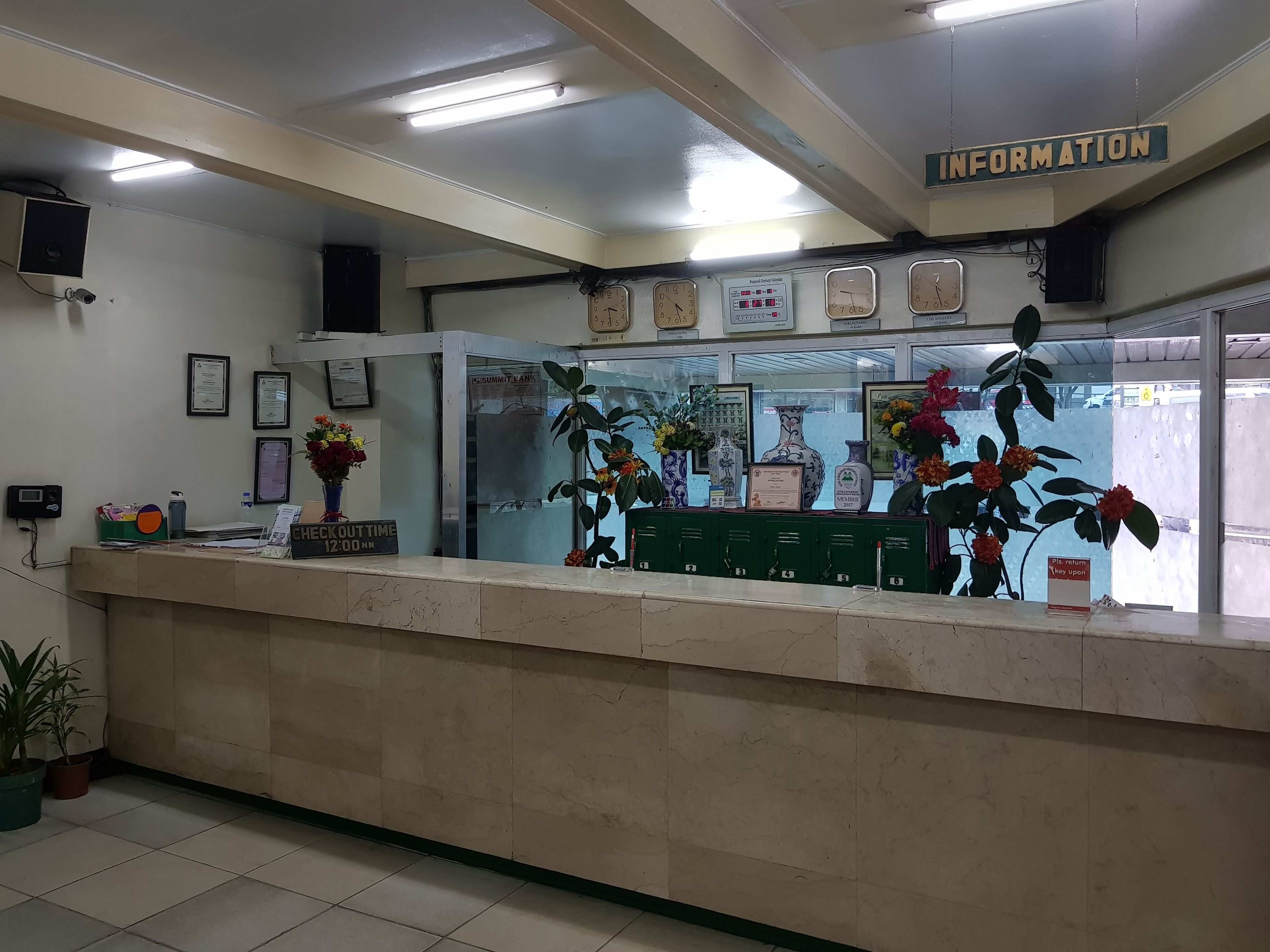 A reception desk with a clock, framed certificates, and a 'Check-out Time 12:00 PM' sign.