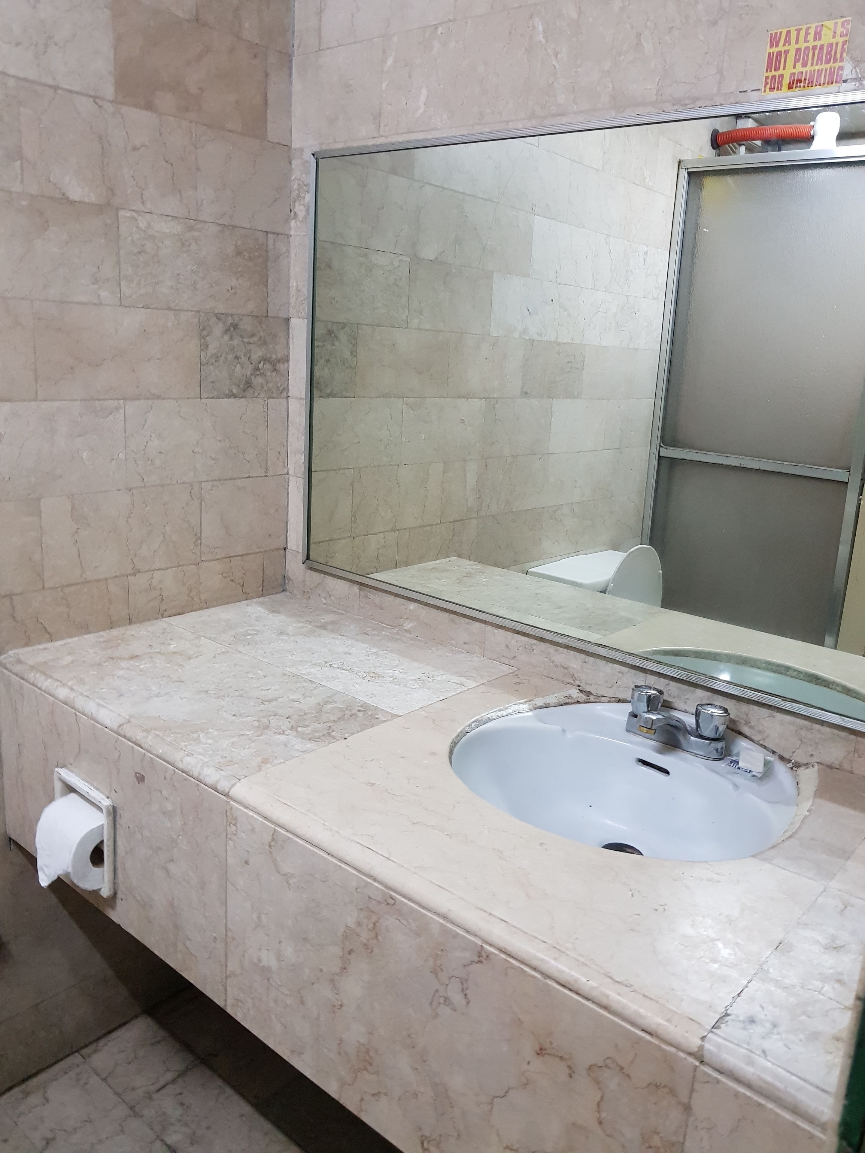 Um banheiro com pia de mármore, espelho e porta-papel higiênico.