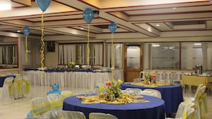 A banquet hall with round tables covered in blue tablecloths, white chairs with yellow sashes, and blue balloons. - Benguet Prime Hotel (Baguio)