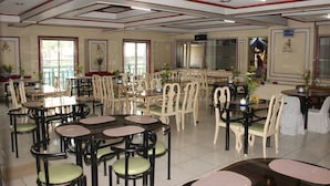 A dining area with multiple tables and chairs, some with green cushions, and a ceiling with red and white beams. - Benguet Prime Hotel (Baguio)