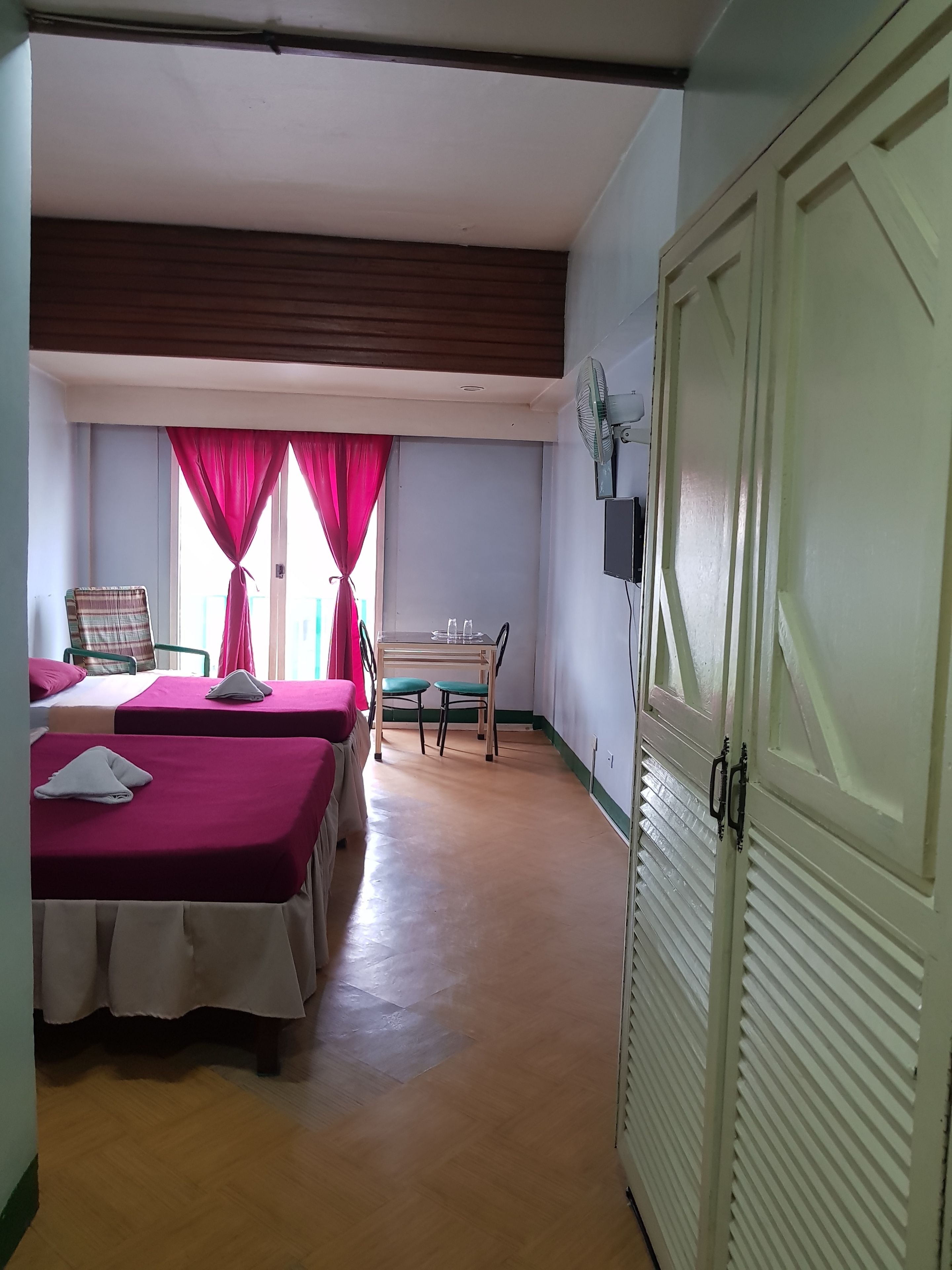 Una habitación con dos camas, una mesa con sillas, un ventilador y un armario.