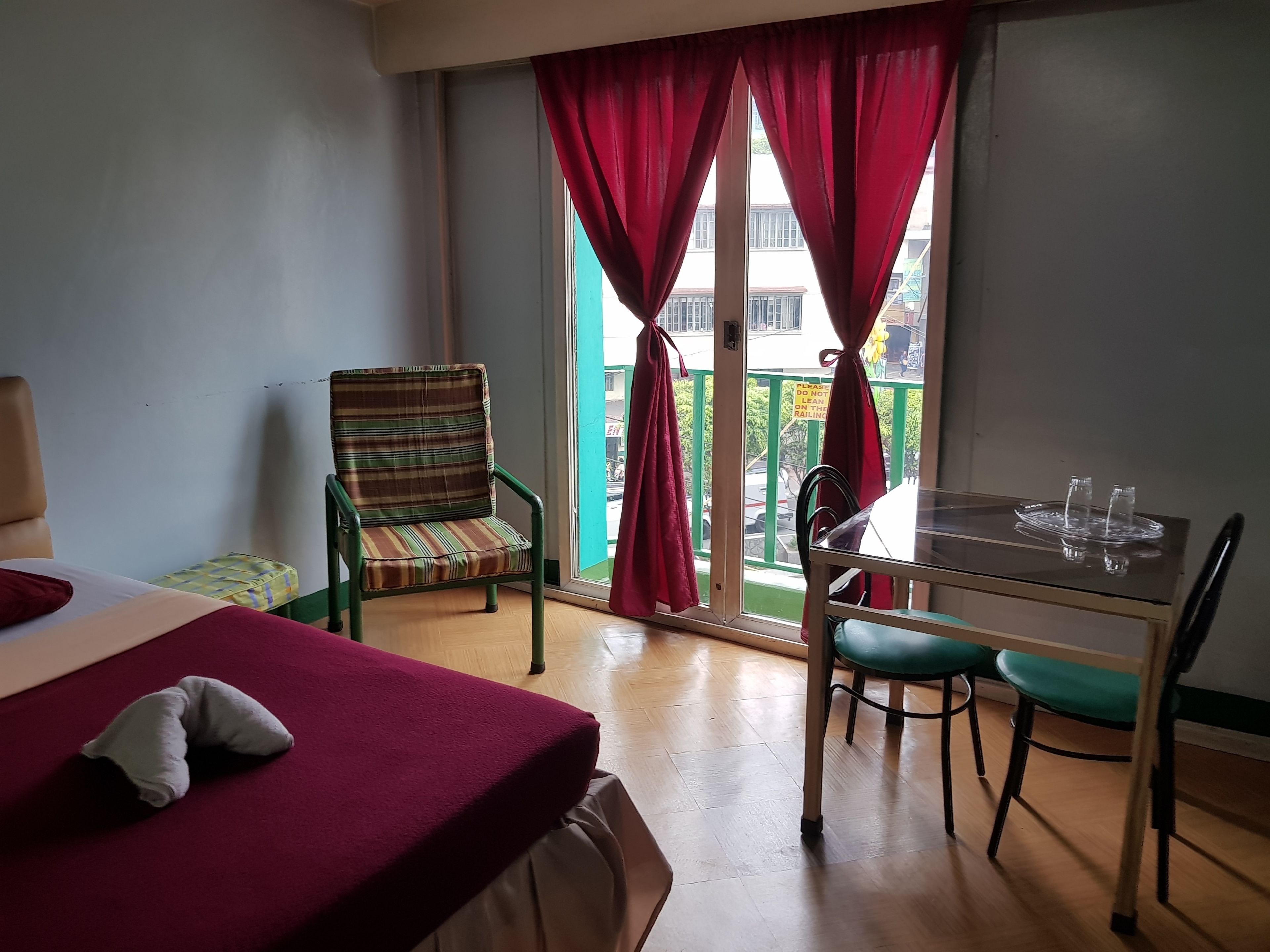 Une chambre d’hôtel avec un lit, une chaise, une table avec des verres et un balcon avec des rideaux rouges.