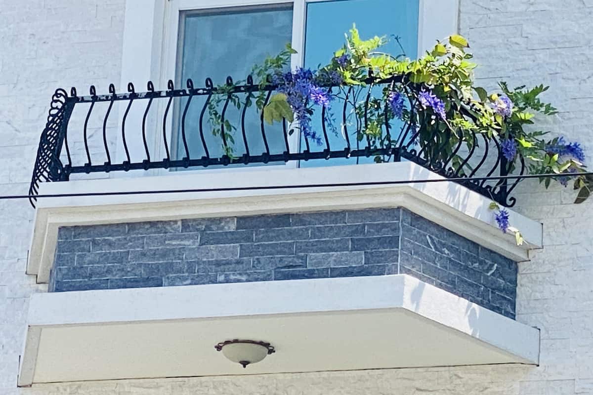 A balcony with a black wrought iron railing, a stone wall, and a window.